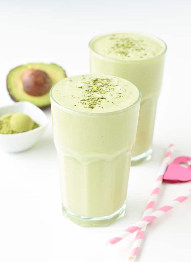 Keto Matcha Smoothie in two large tall glasses with an avocado in the background.