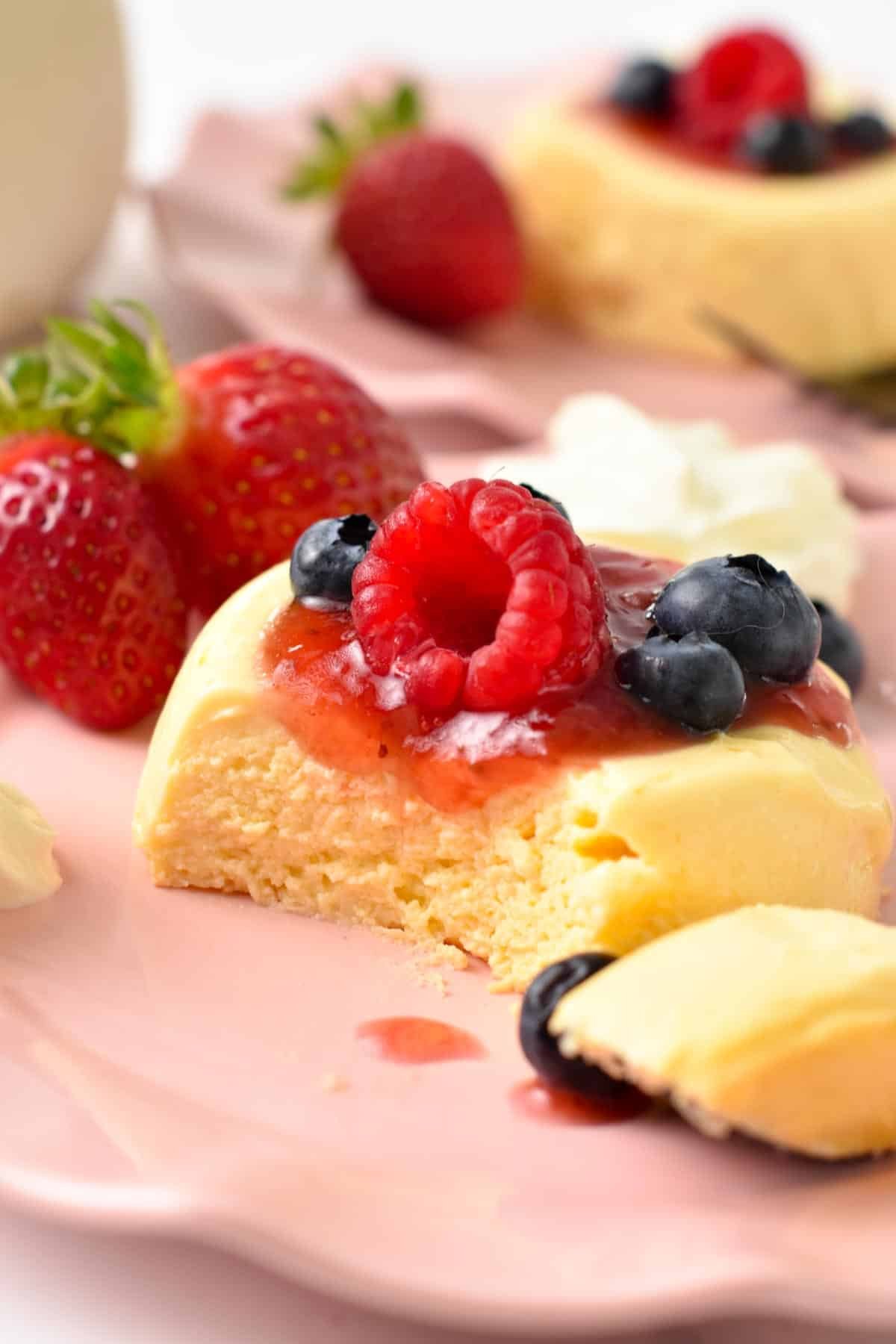 A single-serve microwave cheesecake on a pink plate topped with jam, raspberry, blueberries, and strawberries.