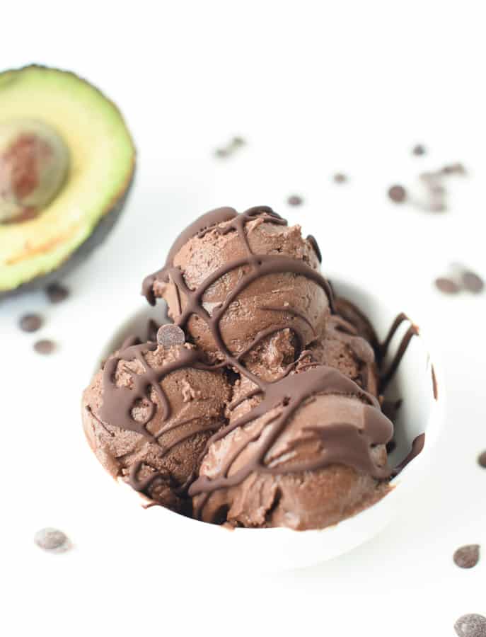 Keto avocado chocolate ice cream served with a drizzle of melted chocolate in front of a halved avocado.
