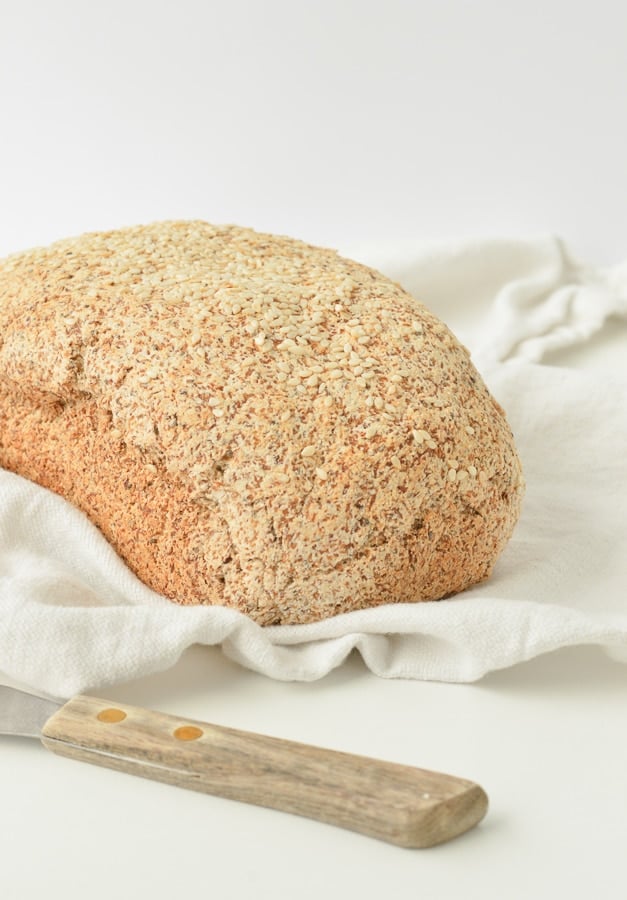 Loaf of eggless keto bread on a kitchen towel next to a small bread knife.