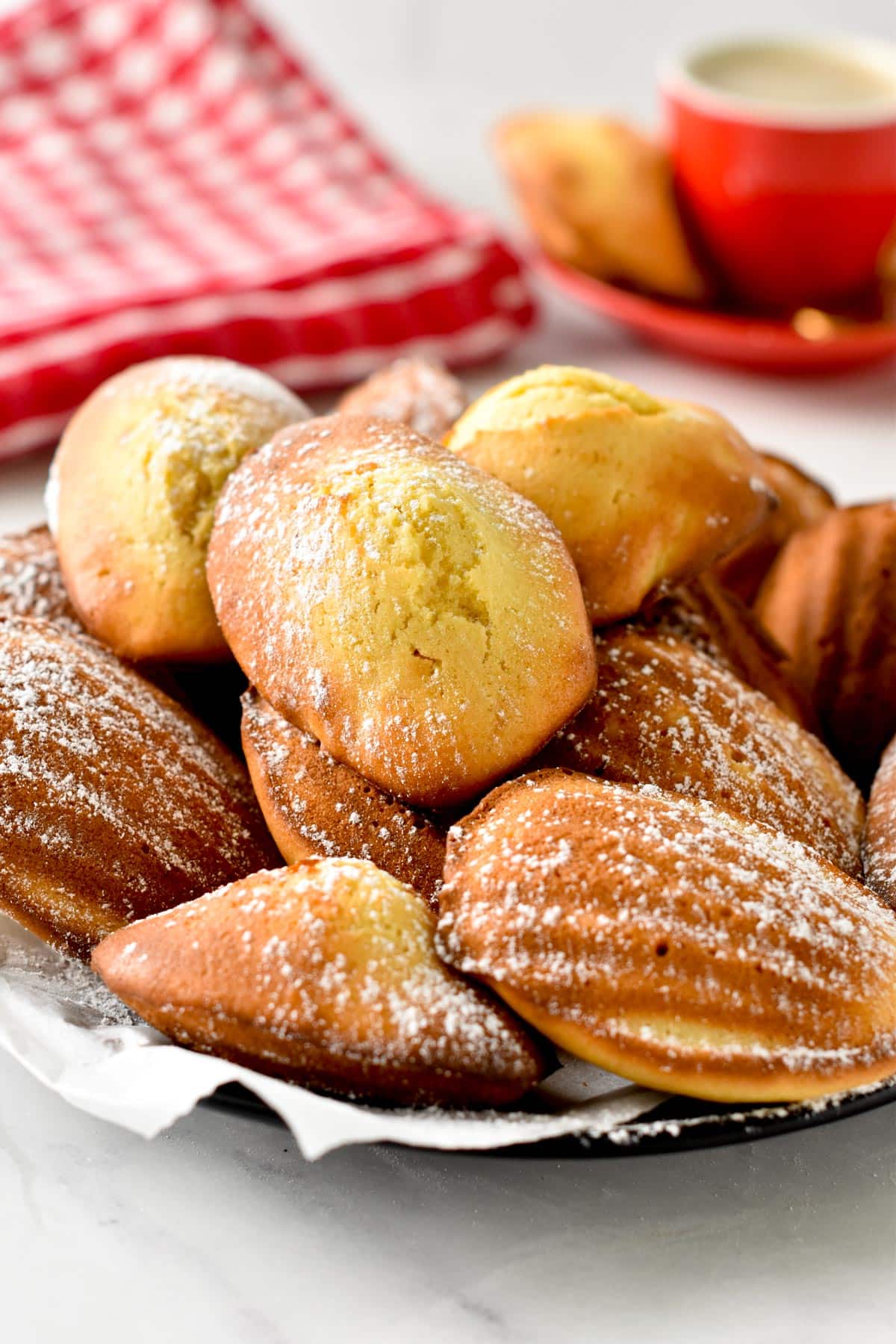 Madeleines stacked on a plate and decorated with powdered sugar.