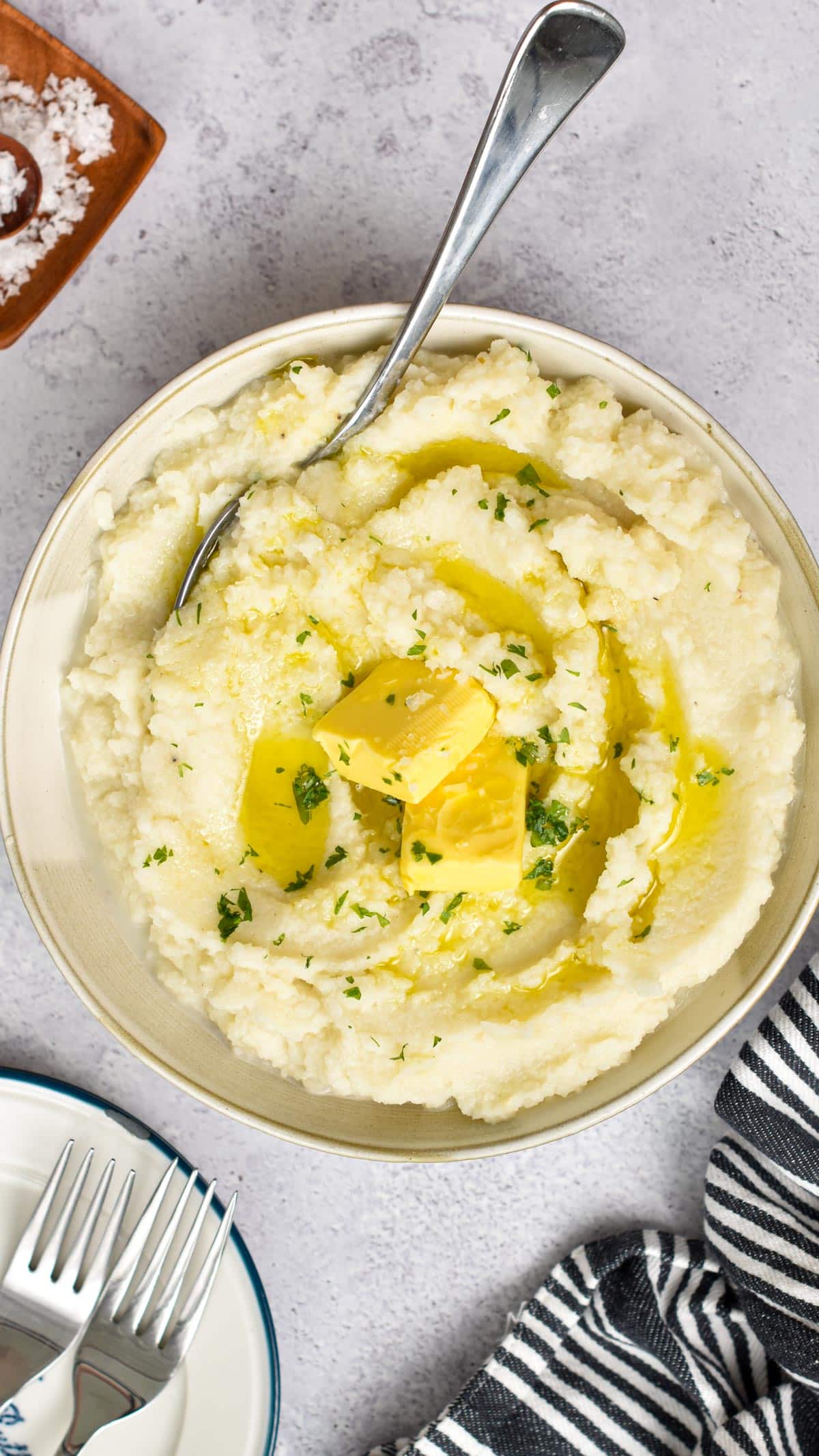 A bowl filled with mashed cauliflower and topped with fresh butter melting in the cauliflower mash, and finely chopped herbs on top.