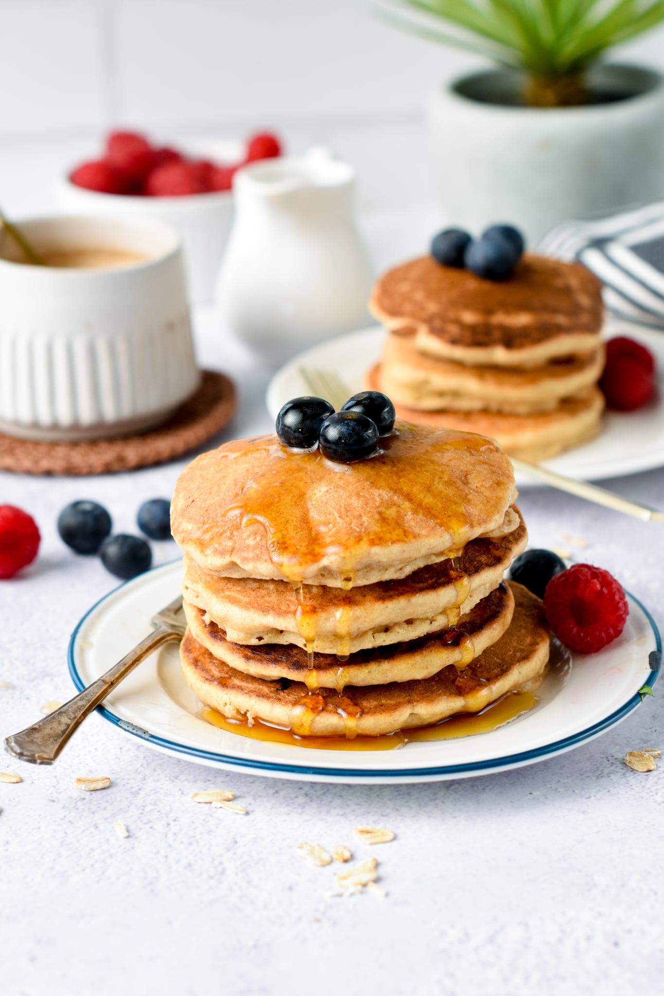 A stack of Oat Flour Pancakes decorated with blueberries and maple syrup.