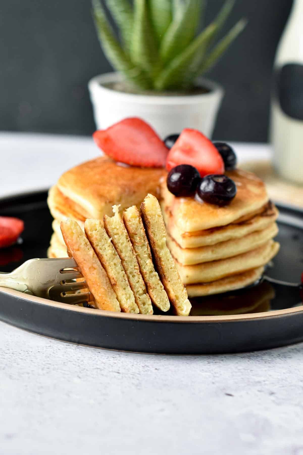 A slice of stacked Paleo Pancakes decorated with strawberries and blueberries on a black plate.