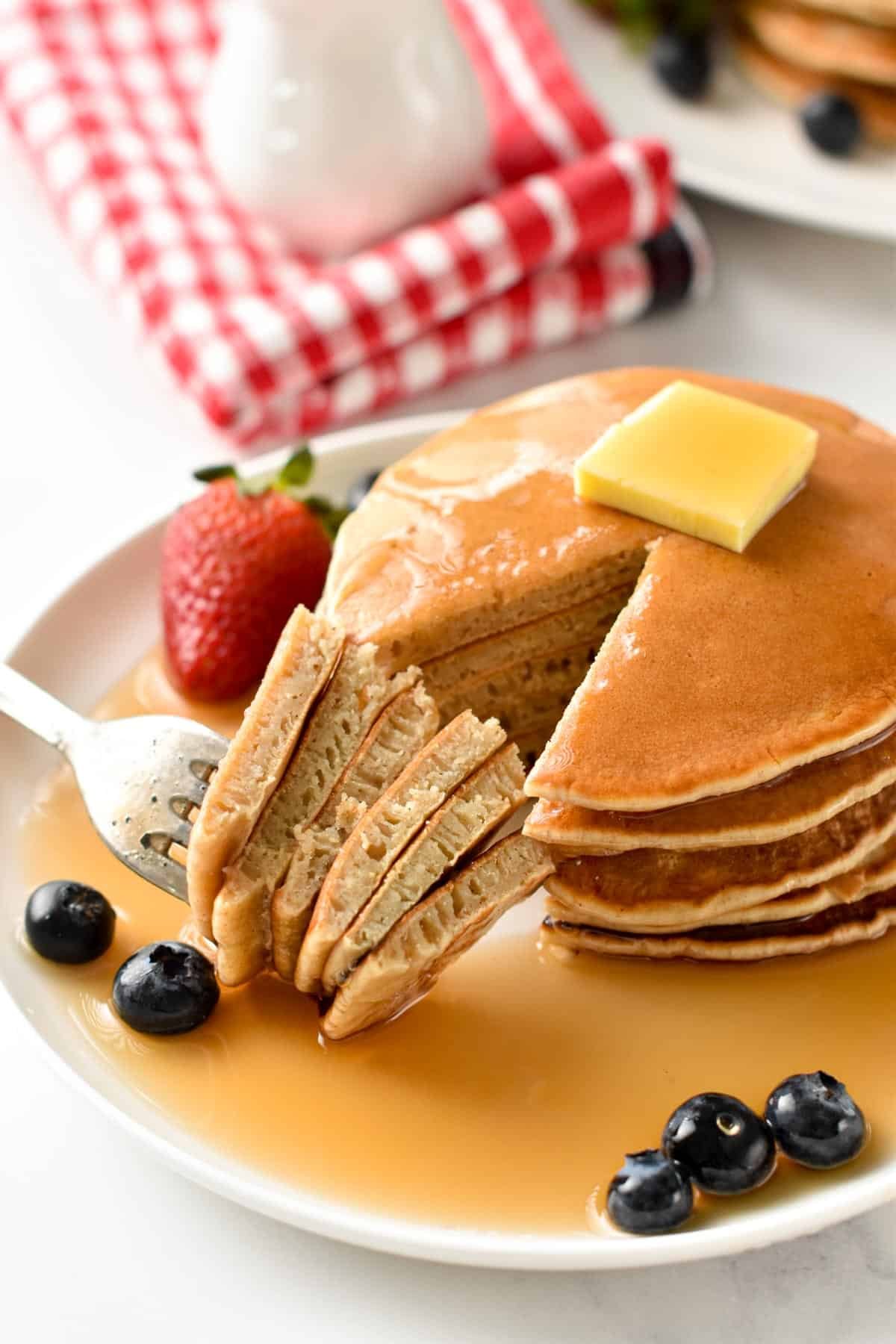 Sugar-Free Pancake stack with a quarter cut and on a fork. Decorated with butter, strawberries, blueberries, and sugar-free maple syrup.