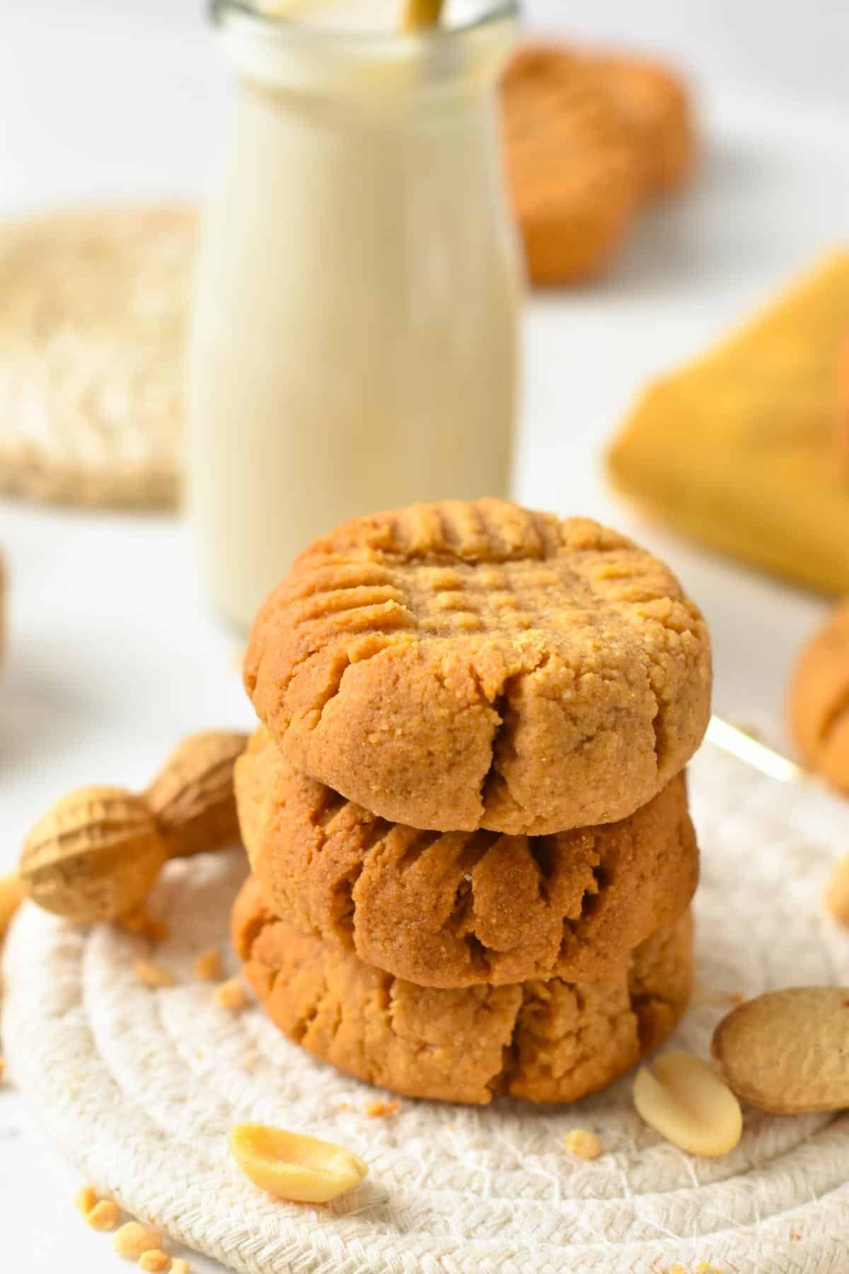 A stack of three peanut butter cookies with a crisscross pattern on top and a bottle of milk in the back.