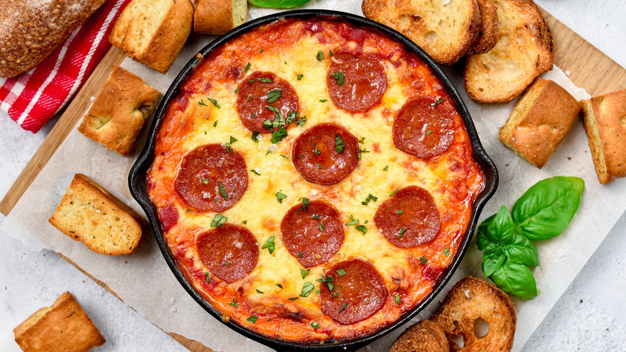 Keto Pizza Dip in a large skillet, surrounded by low-carb bread slices.