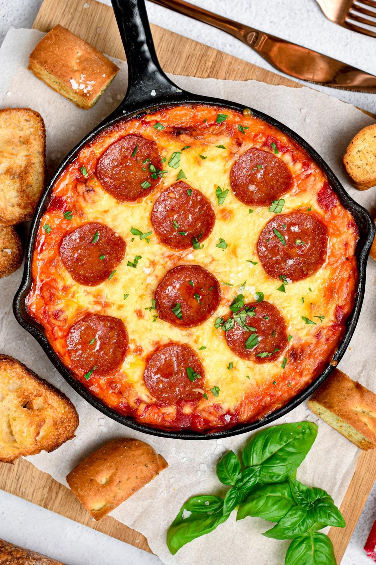 Keto Pizza Dip in a large cast-iron skillet  on a board with basil and low-carb bread slices.