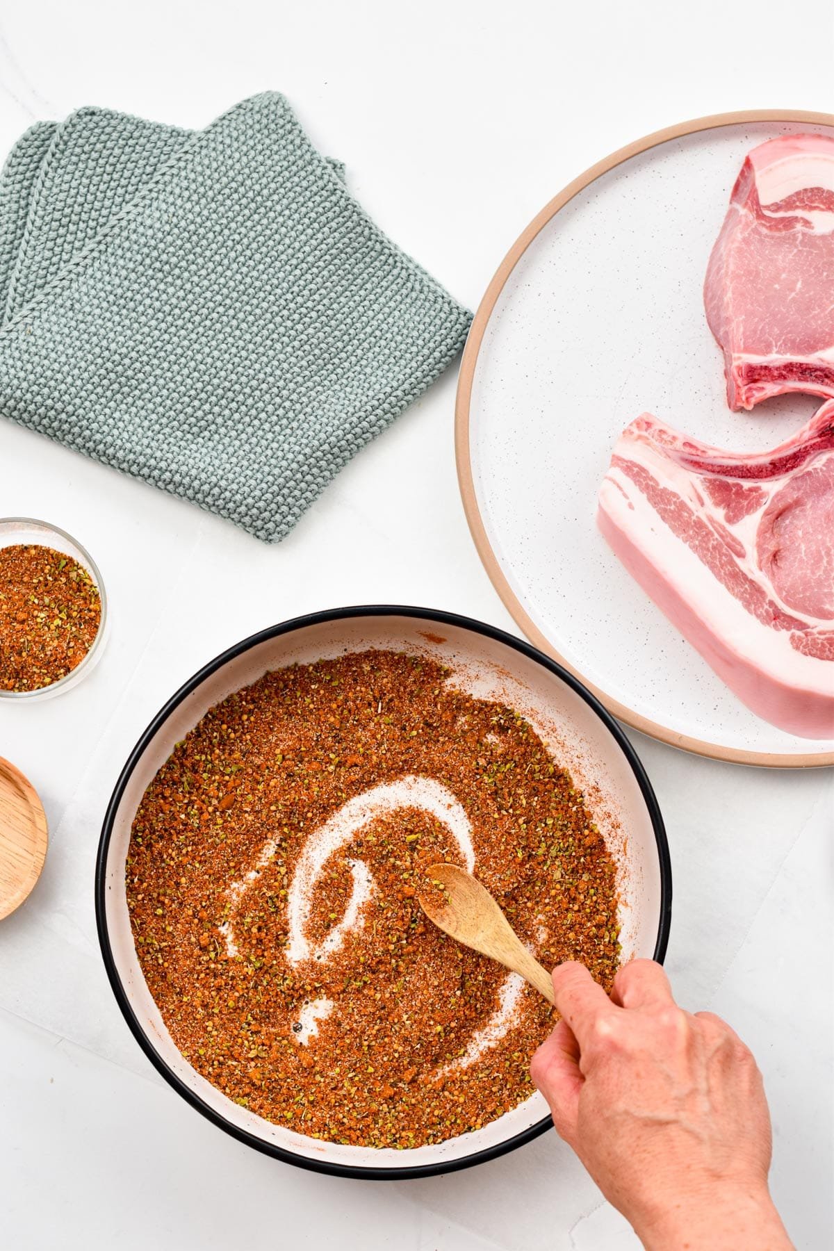 Stirring the pork seasoning ingredients with a wooden spoon on a large bowl next to a plate with pork chops.