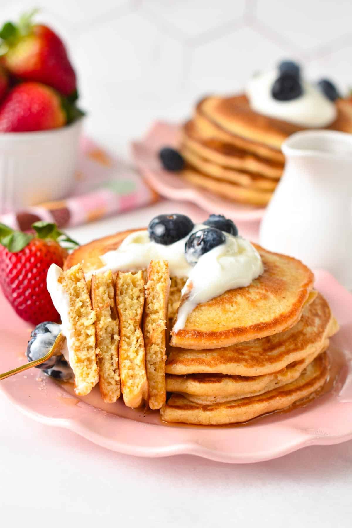 Aa stack of protein pancakes topped with yogurt, blueberries with quarter of it on a golden fork.