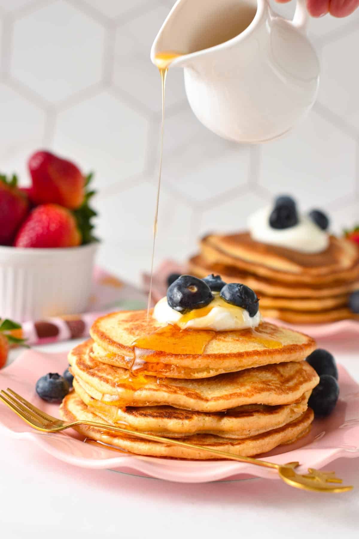 A stack of protein pancakes topped with yogurt, blueberries and as drizzle of maple syrup.