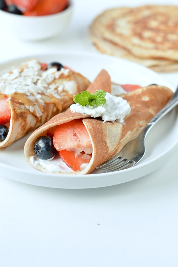 Two Protein Crepes rolled on a plate with fresh fruits and cream cheese.