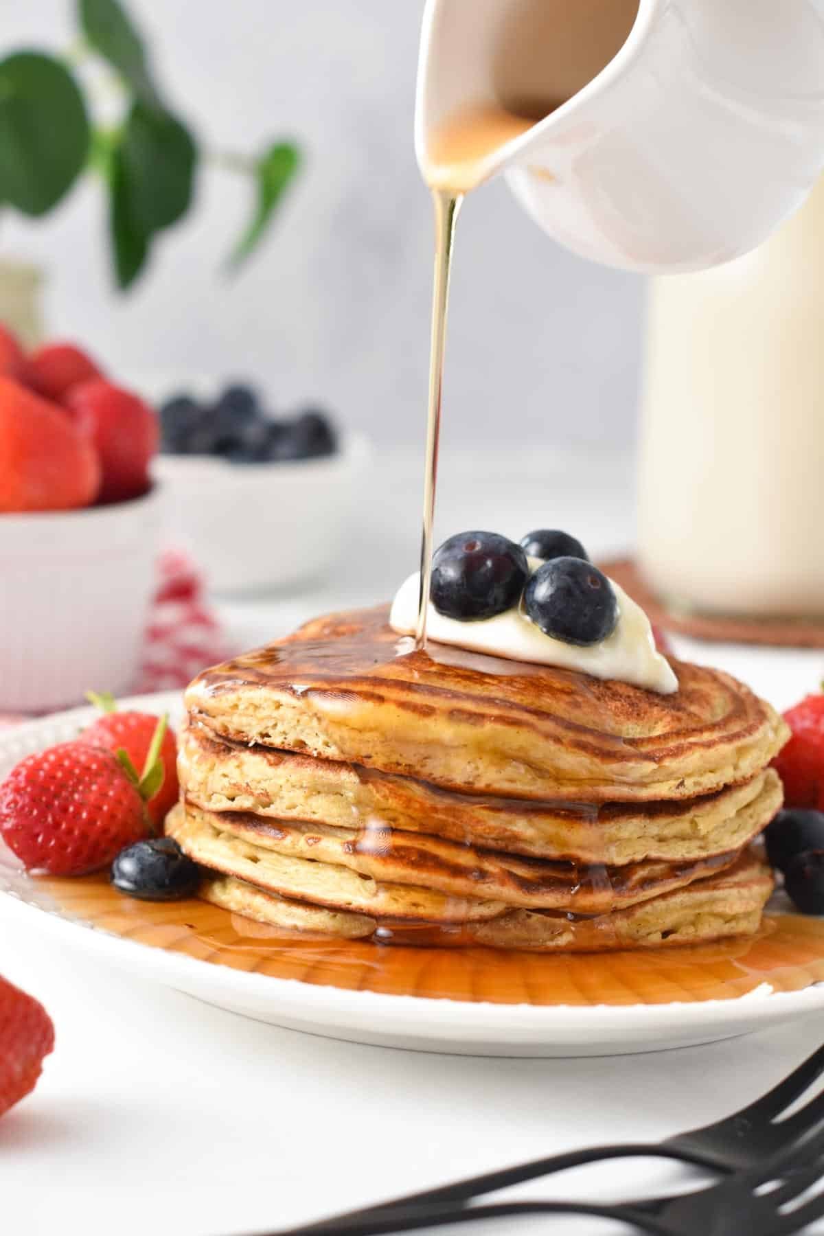 A stack of protein pancakes with Greek yogurt, blueberries on top and a drizzle of maple syrup.