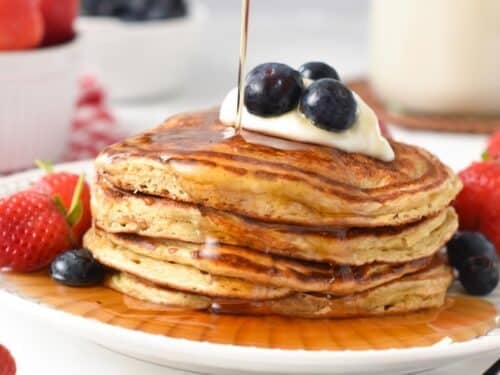 a stack of protein pancakes with Greek yogurt, blueberries on top and a drizzle of maple syrup