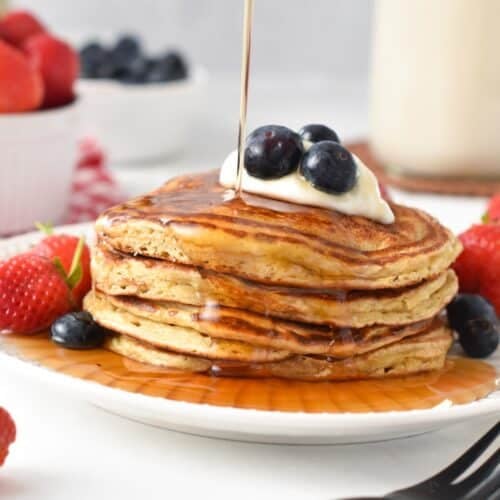 a stack of protein pancakes with Greek yogurt, blueberries on top and a drizzle of maple syrup