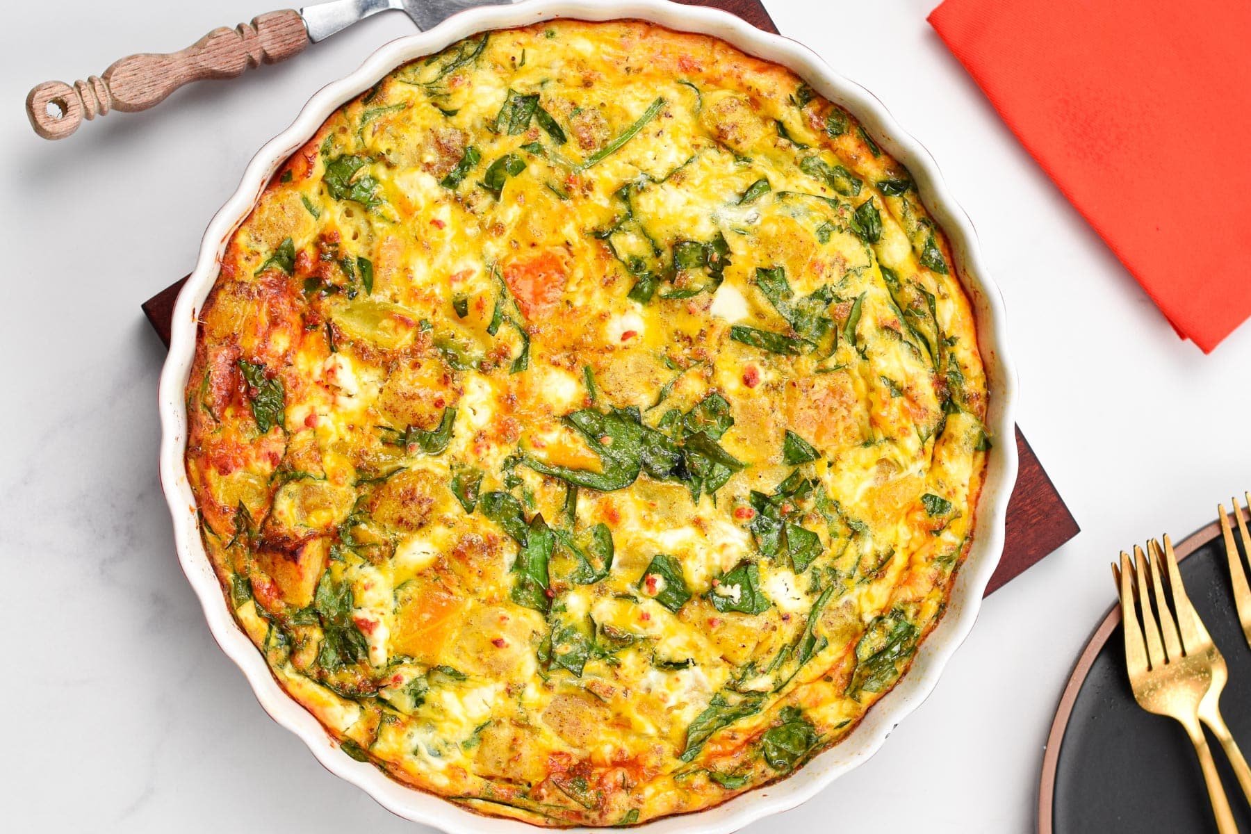 A pie plate filled with baked roasted pumpkin frittata with spinach and feta.