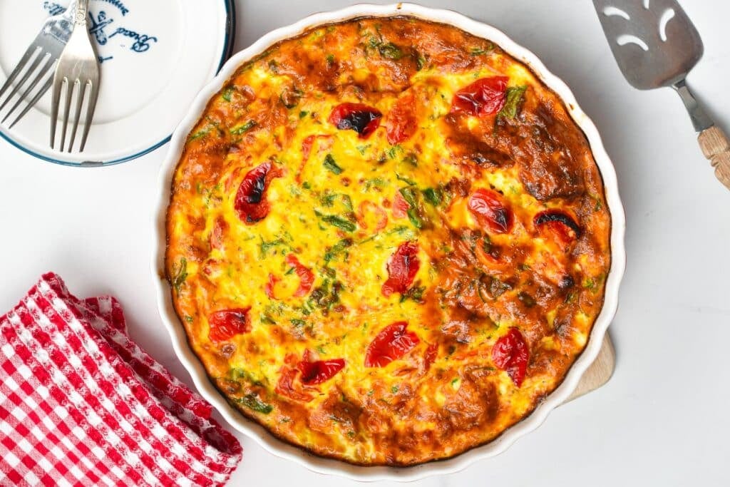 A pie plate filled with ricotta frittata, with roasted bell pepper and spinach.