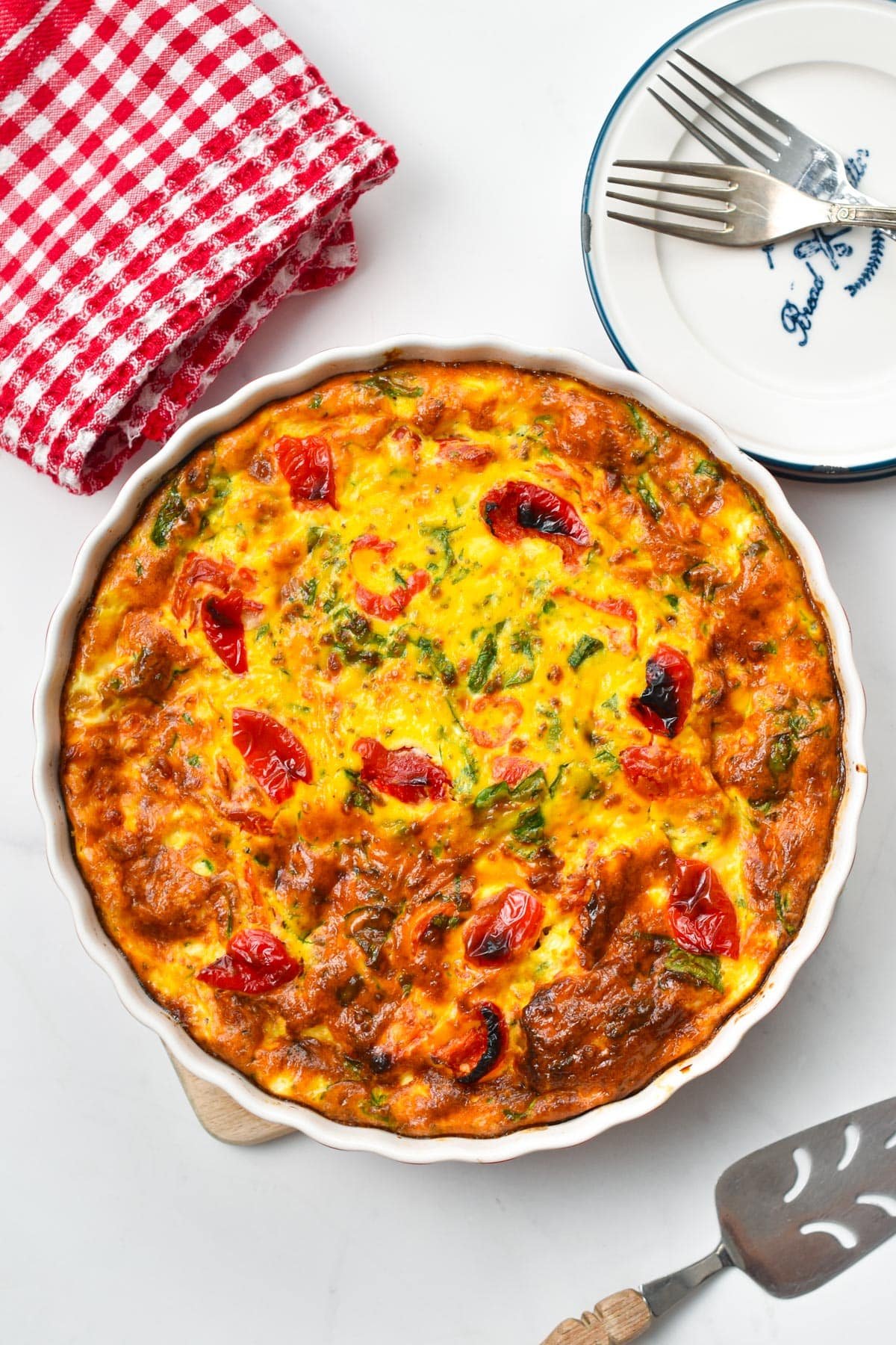 A pie plate filled with ricotta frittata, with roasted bell pepper and spinach.