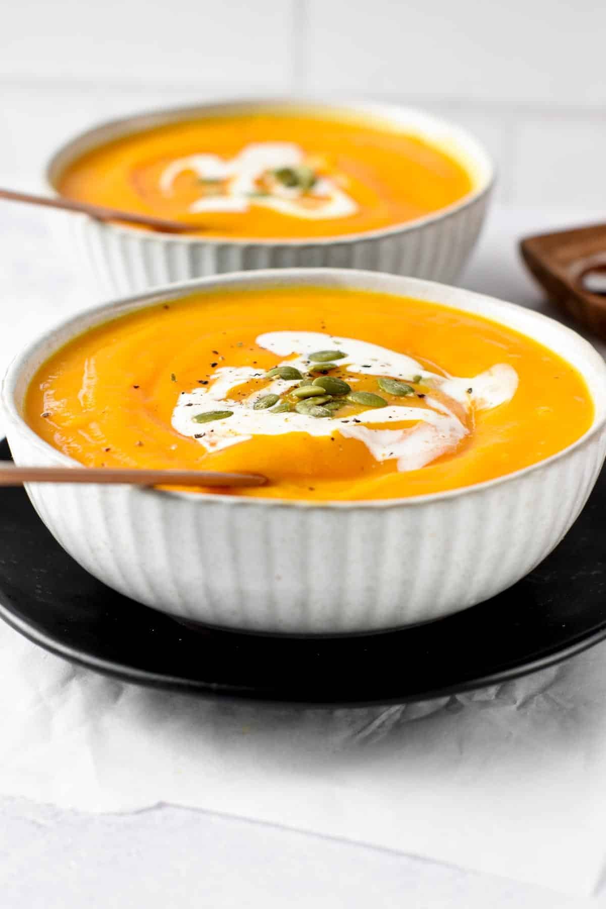 Two bowls of Butternut Squash Soup topped with cream and pumpkin seeds. 