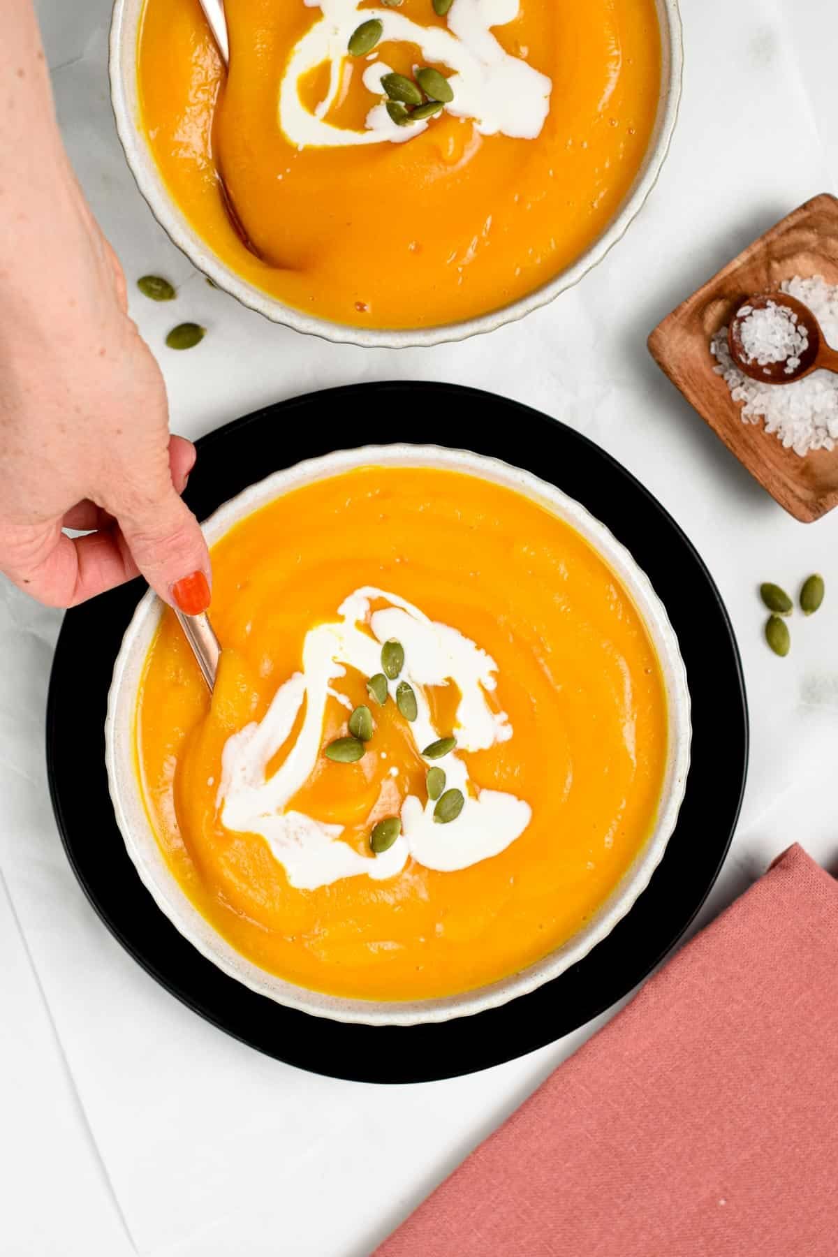 3-ingredient Butternut Squash Soup in a white bowl on a black plate, stirred with a spoon.