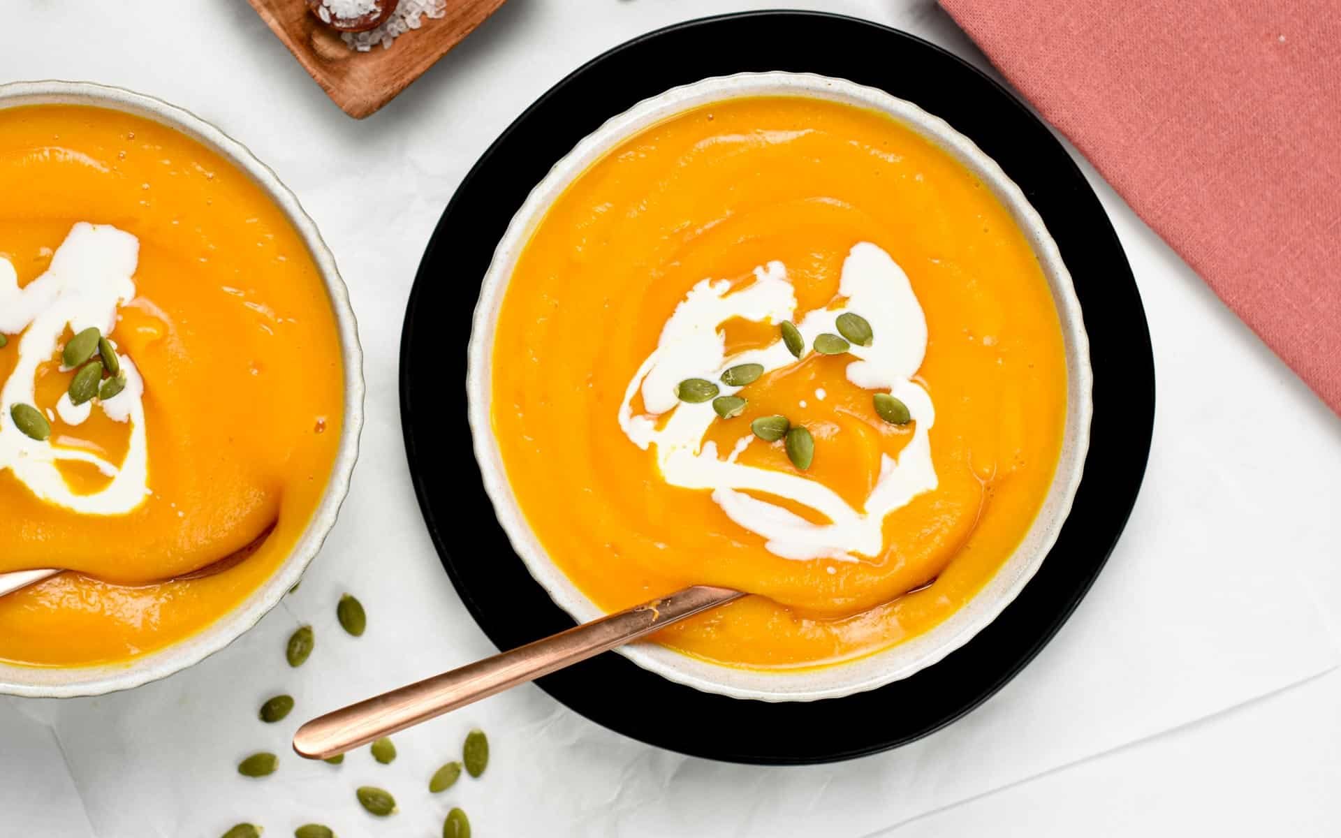 Serving of Butternut Squash Soup in a white bowl, decorated with cream and pumpkin seeds.