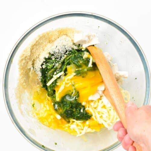a glass bowl with a wooden spoon stirring Spinach Fritters Batter with eggs, cheese, spinach, almond flour