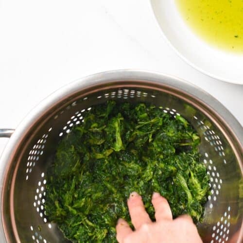 a hand pressing thawed spinach over a sieve to remove excess water
