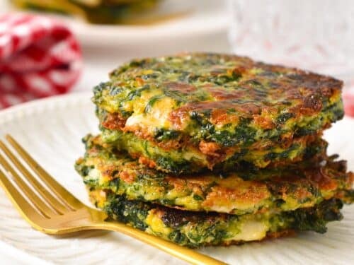 a stack of spinach fritters on a white plate with a golden fork in the front