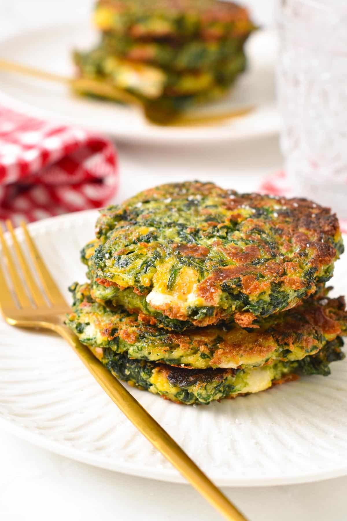 A stack of spinach fritters on a white plate with a golden fork in the front.