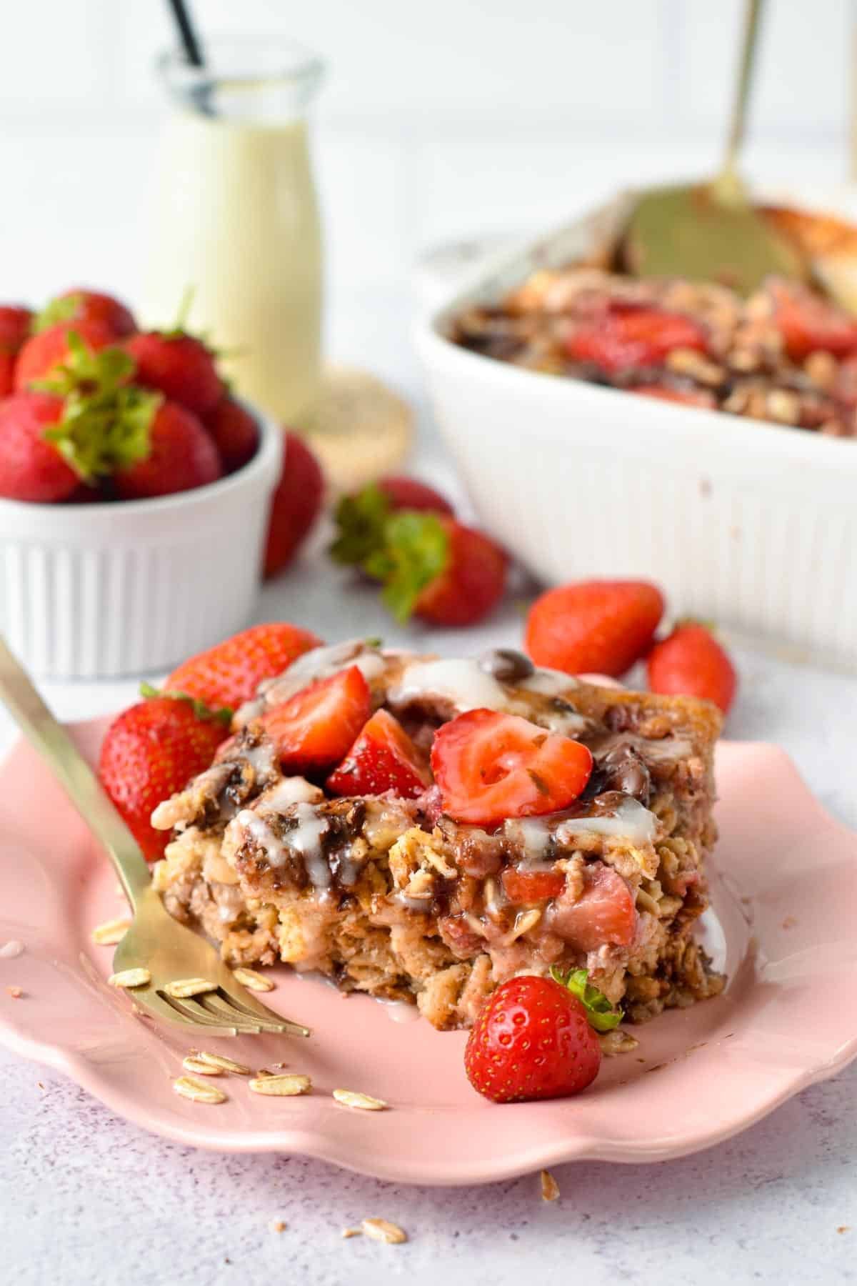 Strawberry Baked Oatmeal slice on a pink plate with a golden fork.