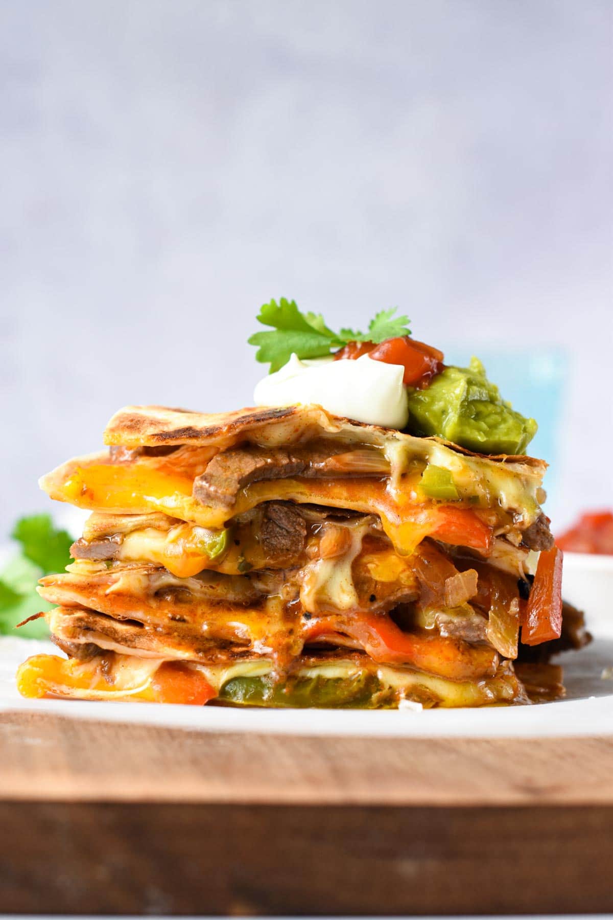 Steak Quesadilla sliced in quarters, stacked on a plate and decorated with guacamole, cream, and cilantro. 