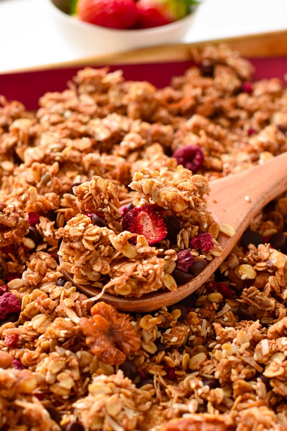 A wooden spoon filled with granola sitting on a large batch of baked homemade granola.