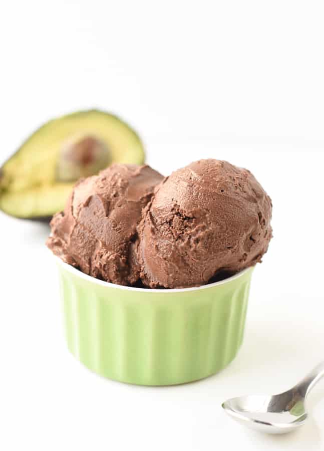 Chocolate avocado ice cream in a small green ramekin in front of a sliced avocado.