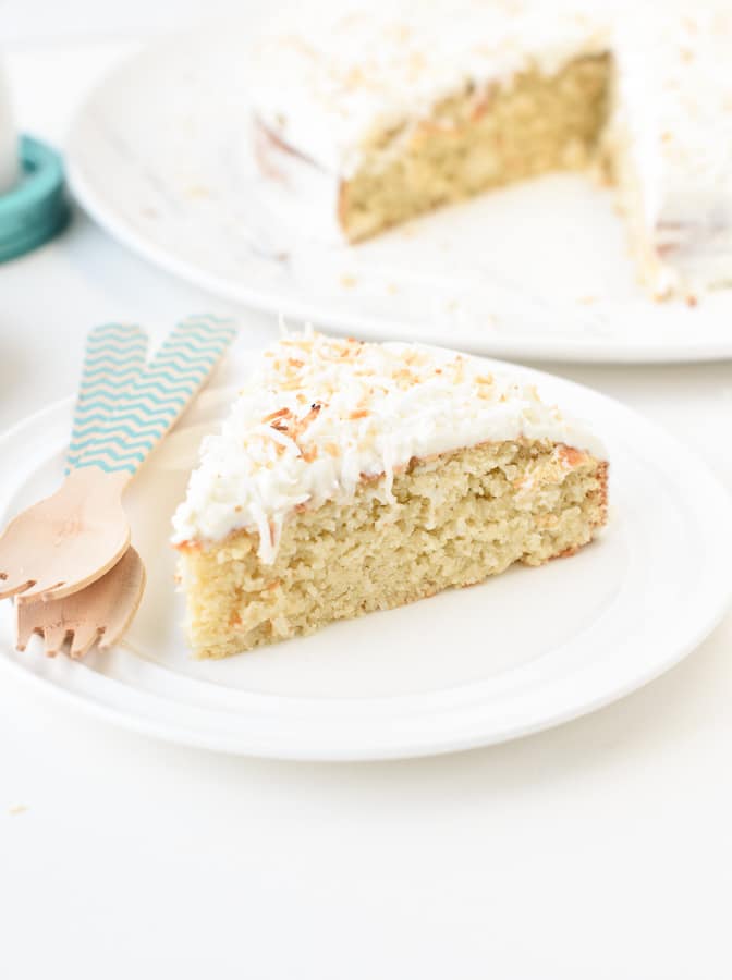 A slice of coconut cake on a plate with bamboo forks.